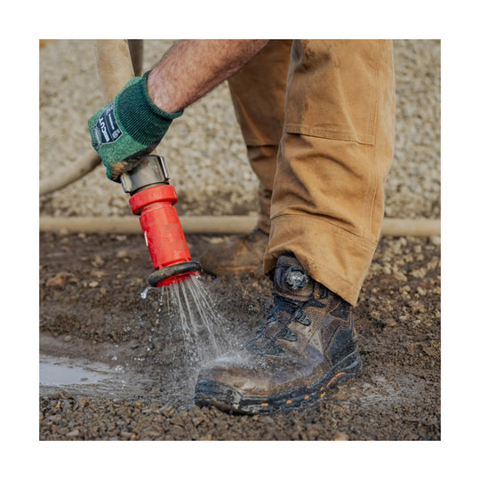 Mud-splashed brown and black work boot with BOA dial, being rinsed with water