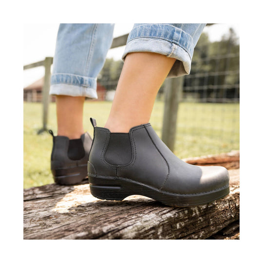 Black Chelsea-style ankle boots with low wedge soles, worn with rolled-up jeans outdoors
