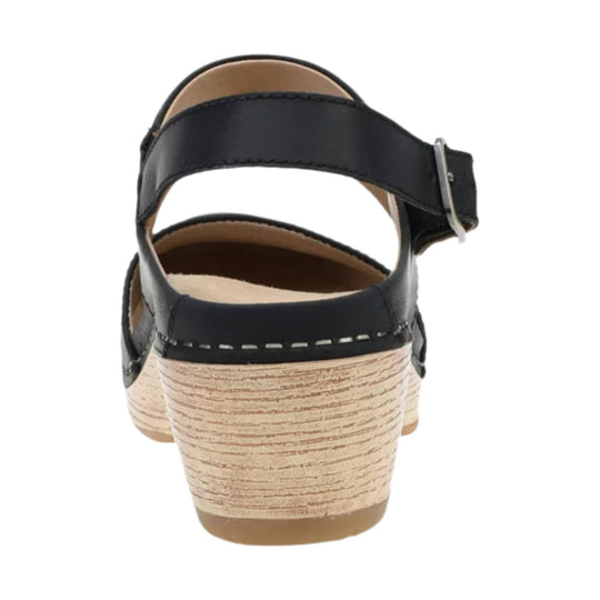 Black strappy sandal with a silver buckle and woodgrain wedge heel, rear view
