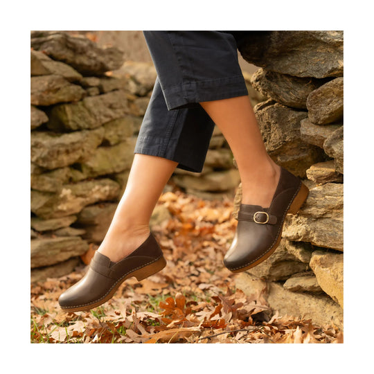 Brown leather clogs with low wooden heels and buckle straps, worn outdoors on rocks