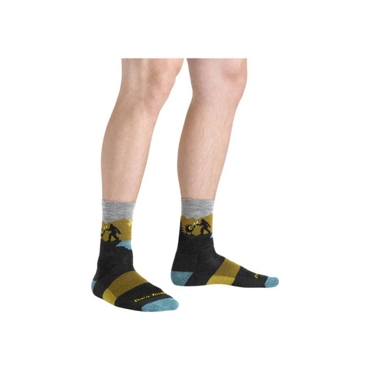 Black hiking socks with mustard yellow and light blue accents, shown on a model wearing them