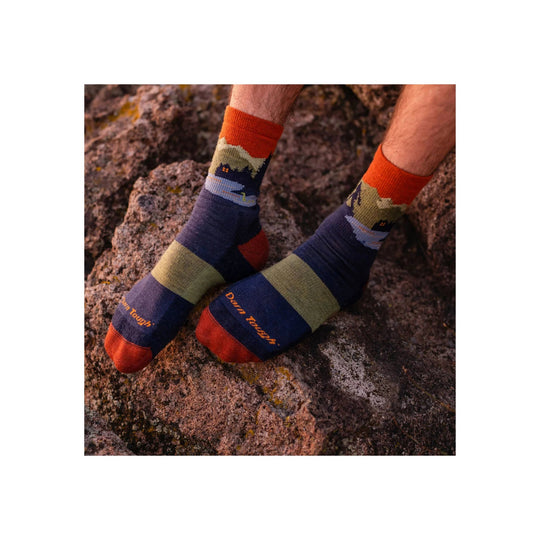 Pair of multicolor hiking socks worn on feet against rocky terrain, with visible Darn Tough text