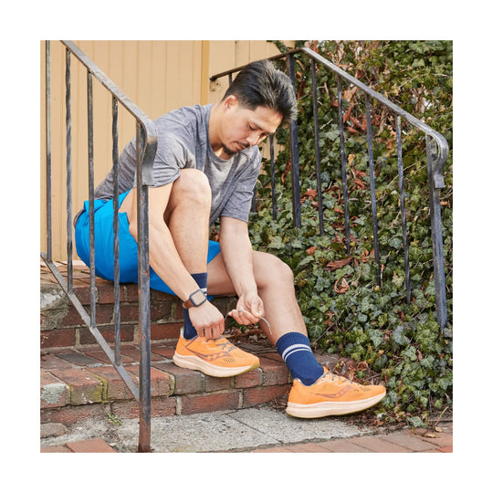 Orange running shoes with white soles worn with navy socks, shown while being laced on outdoor steps