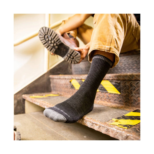 Dark gray crew sock worn on a person sitting on metal stairs