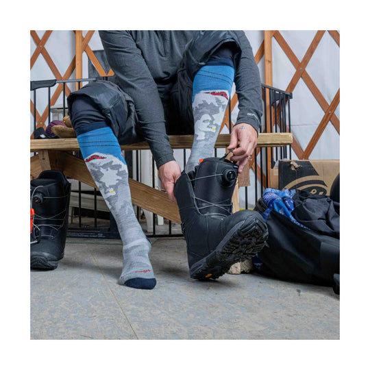 Gray ski socks with blue cuffs and a camo face pattern being put on with black snowboard boots