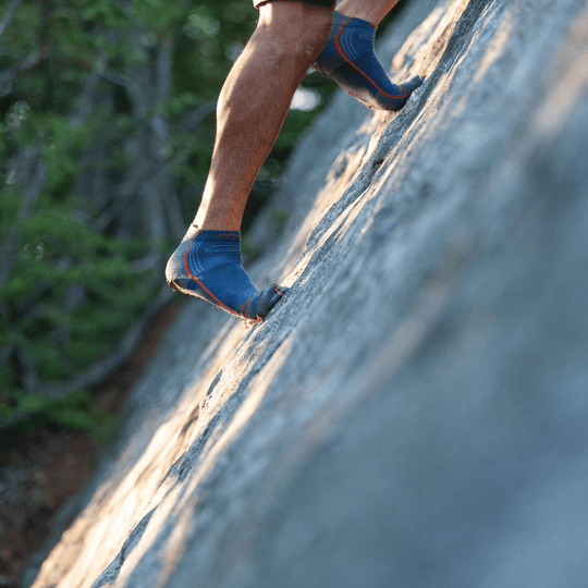 Blue low-cut hiking socks on a climber’s feet on a granite rock face
