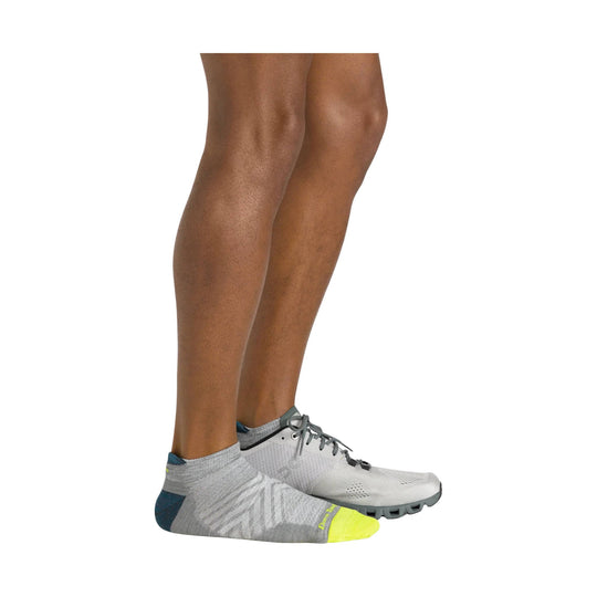 Gray no-show running sock with a neon yellow toe and heel tab, shown on a model foot next to a white running shoe.