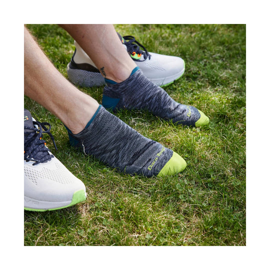 Dark gray low-cut running sock with a neon green toe and blue heel, worn with white running shoes on grass.