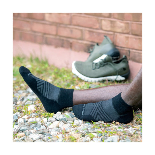 Black ankle running socks with gray geometric pattern, shown on a person lying on gravel beside running shoes