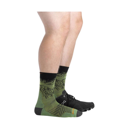Olive green patterned socks with black toe, heel, and cuff on a model wearing black shoes