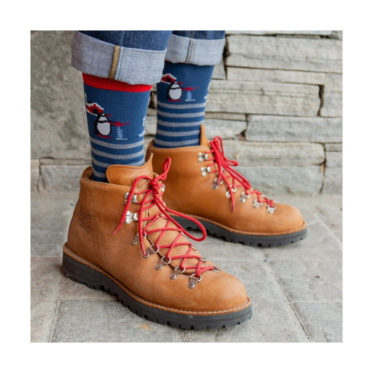 Tan leather hiking boots with red laces and metal hooks, worn with blue striped socks featuring a penguin.