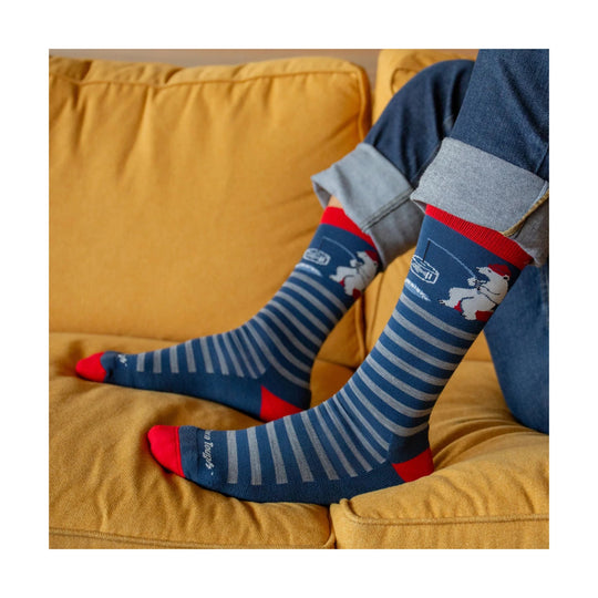 Blue and gray striped crew socks with a polar bear graphic and red toes and heels, worn with cuffed jeans on a yellow couch.