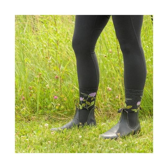 Black ankle rain boots with floral crew socks, worn with black leggings in a grassy field