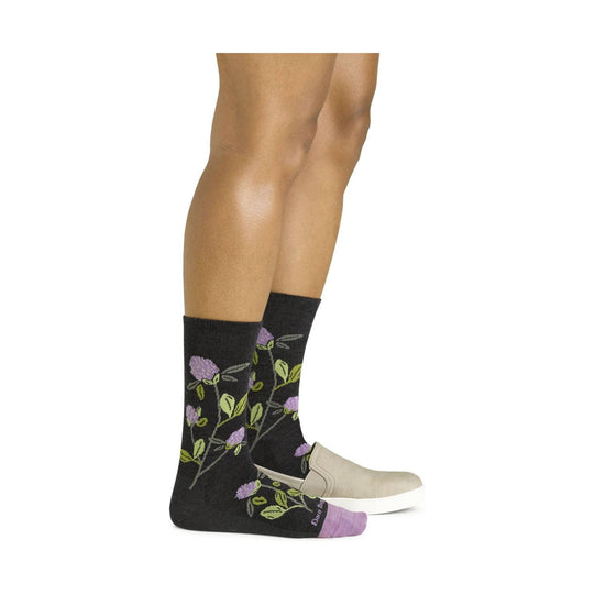 Black crew socks with purple and green floral pattern on a model wearing beige slip-on shoes