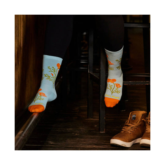 Light blue crew socks with orange flower pattern and orange toes, worn with brown boots