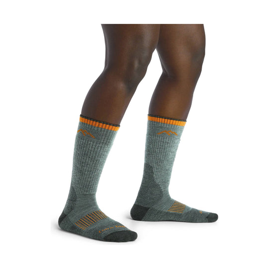 Gray knee-high hiking socks with orange stripes and mountain logo, shown on model’s lower legs and feet