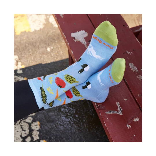 Light blue crew socks with green toes and farmer's market graphics, worn on crossed feet