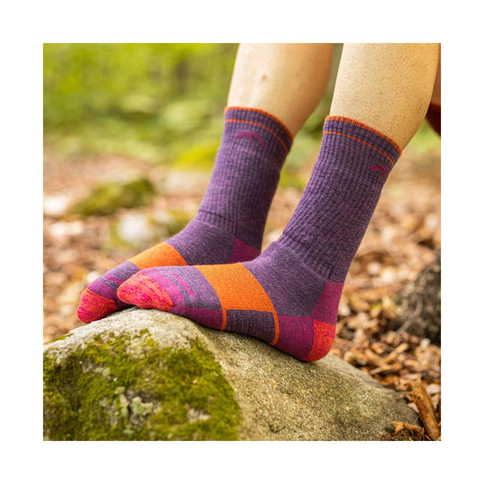 Purple and orange ribbed hiking socks on feet standing on a mossy rock