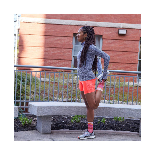 Pink and coral striped running crew sock on a runner stretching outdoors