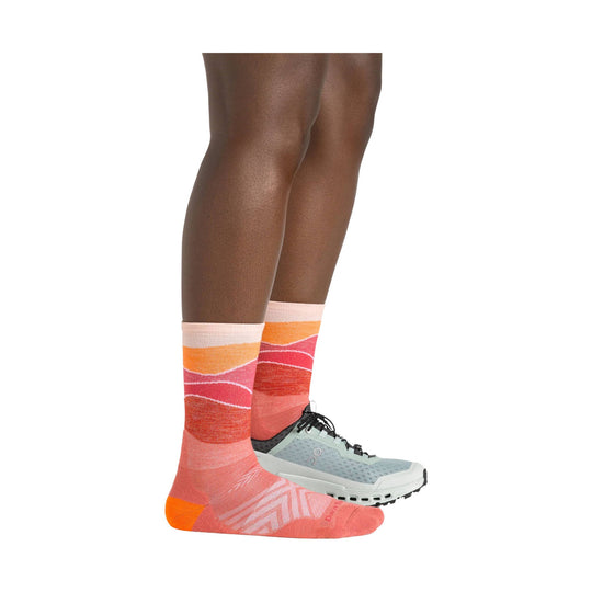 Coral, orange, and pink patterned crew socks worn with a gray trail running shoe