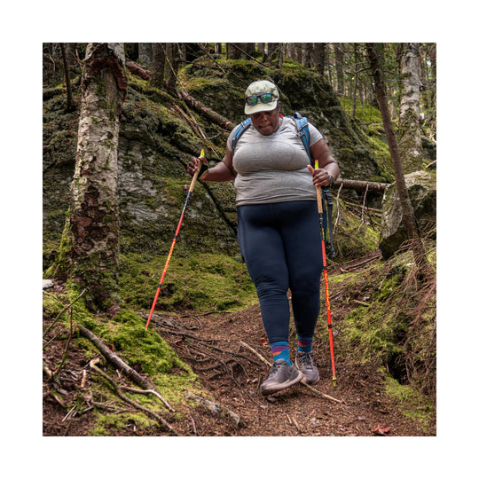 Trail hiker wearing colorful crew socks, gray running shoes, and trekking poles on a wooded path