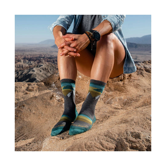 Teal and gray patterned crew hiking socks worn outdoors on rocky terrain