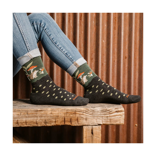 Patterned crew socks with mushroom and hedgehog design, worn with cuffed jeans on a wooden bench