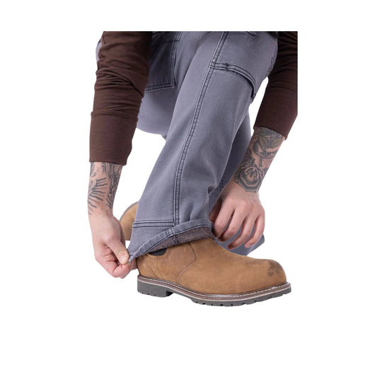 Grey work pants cuffed over a brown leather work boot, with hands adjusting the hem.