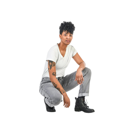 Woman crouching in light gray pants, white V-neck T-shirt, and black lace-up boots on a white background