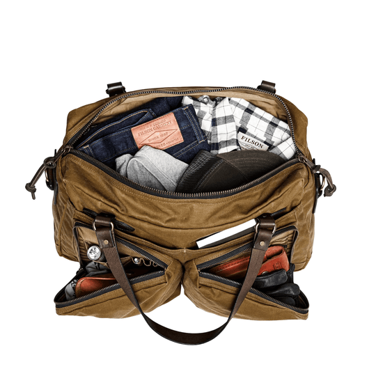 Brown canvas duffle bag open with folded clothes inside, leather straps, and Filson tags visible