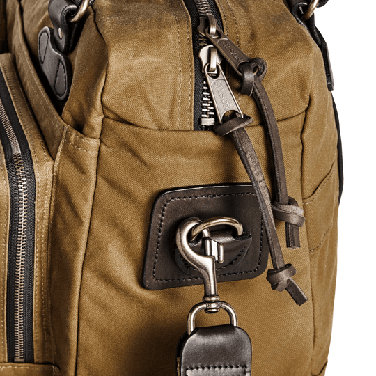 Tan canvas duffle bag with leather trim, zipper pulls, and hanging metal clip