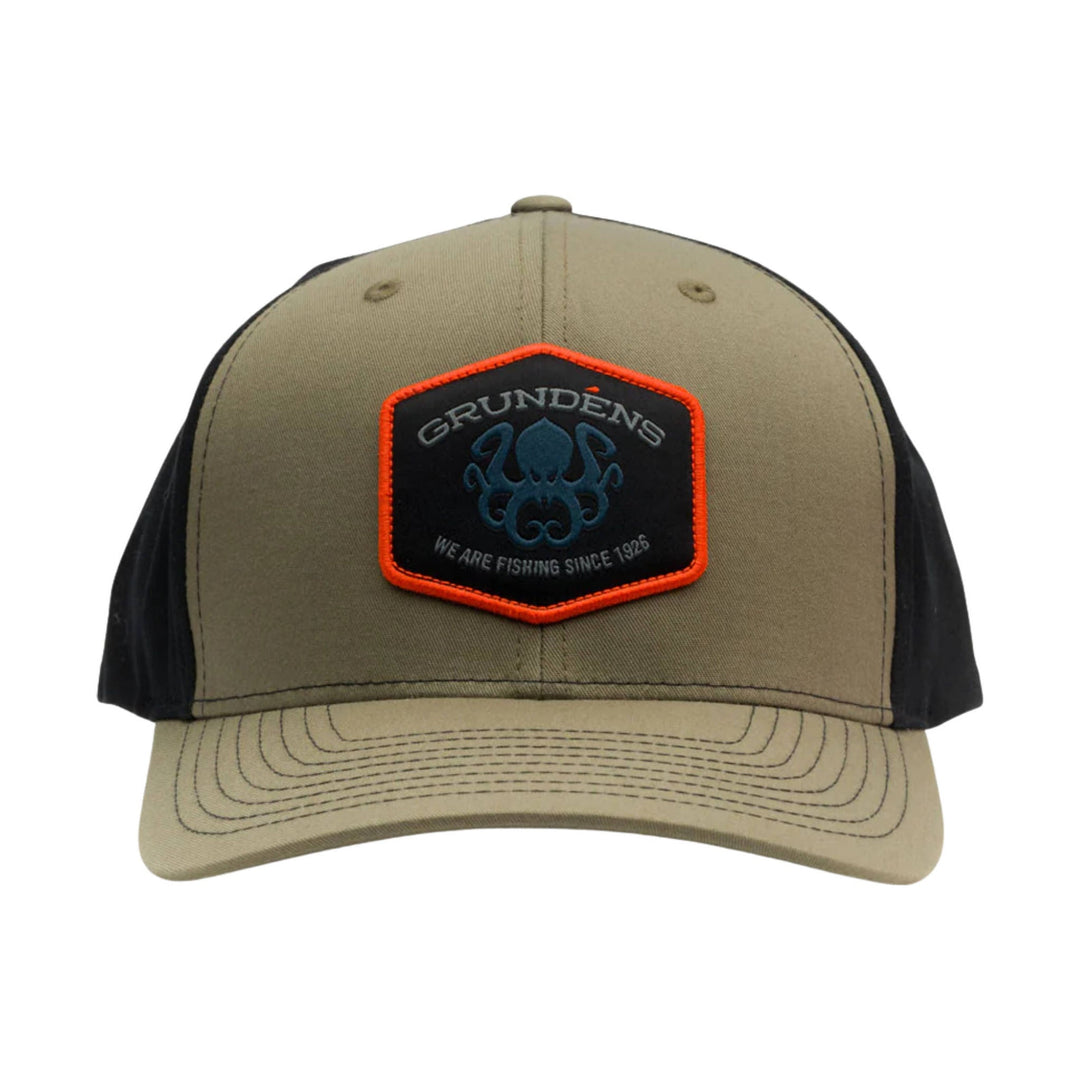 Tan and black trucker hat with a hexagonal front patch and orange trim