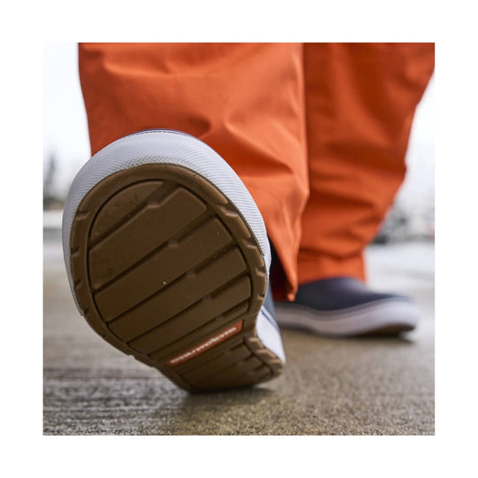 Close-up of a navy boot sole with brown tread, worn by someone in orange pants