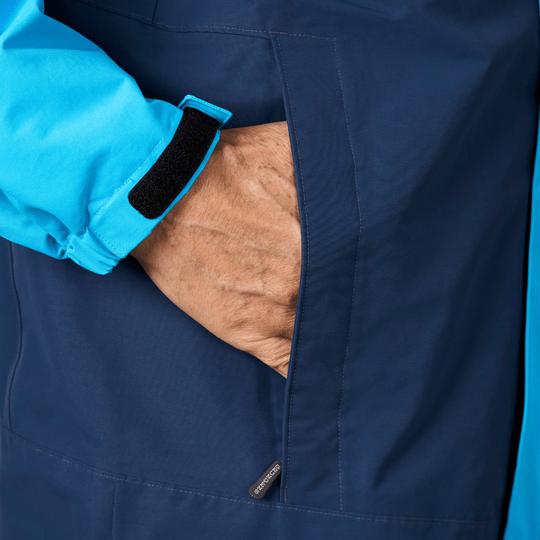 Navy jacket with bright blue cuff, hand in zippered pocket, and hook-and-loop wrist tab