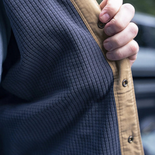 Close-up of a navy quilted shacket with tan snap placket being held by a hand