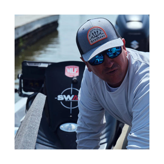 Heather gray and black trucker cap with a fishing patch on the front, worn by a man on a boat.