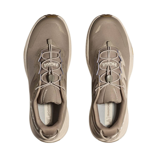 Taupe pair of low-top trail shoes with bungee laces, mesh uppers, and "TRANSPORT" text on the insoles.
