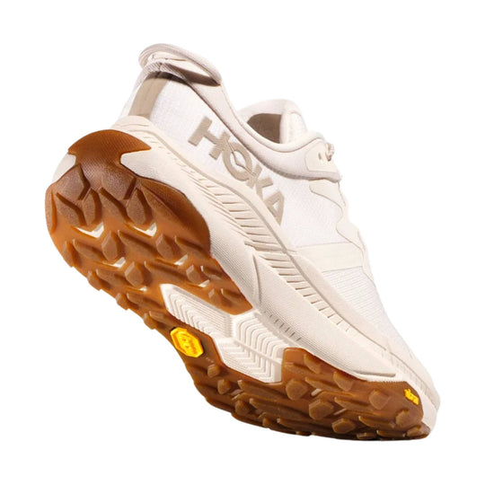 Cream low-top trail shoe with a brown lugged outsole and side logo, shown from the bottom angle.