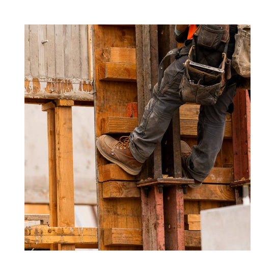 Brown leather work boots with light soles worn by a construction worker on wooden framing