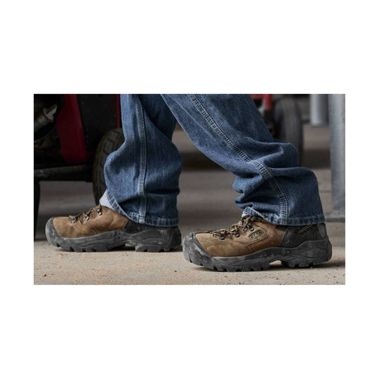 Brown and black leather work boots with rugged lug soles, worn with blue jeans