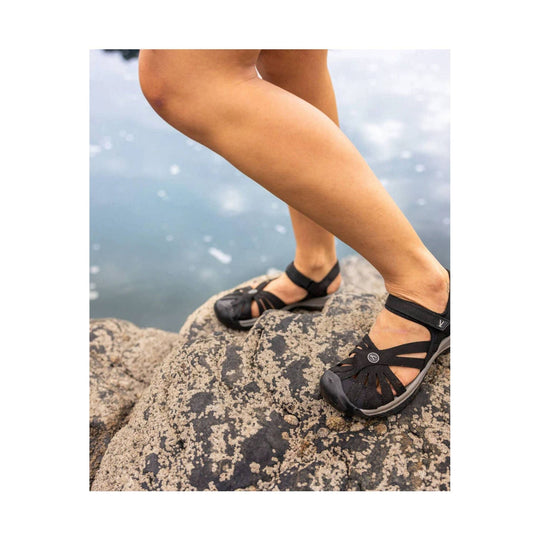 Black strappy closed-toe sandal on a foot standing on rocks