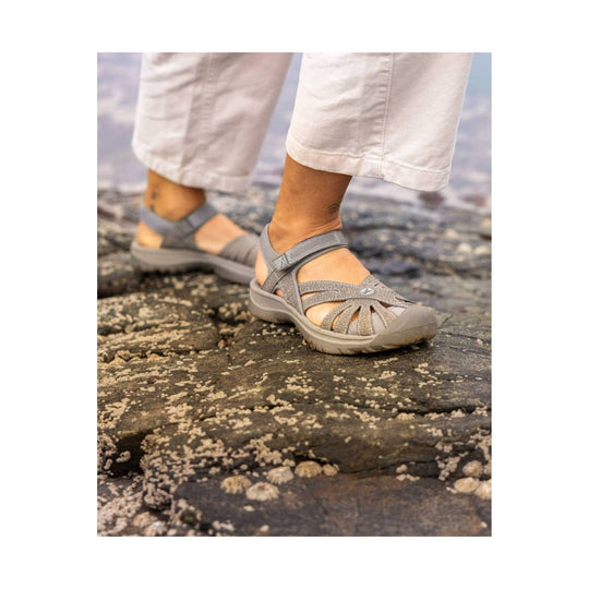 Gray closed-toe walking sandal with crisscross straps and hook-and-loop heel strap on rocky ground