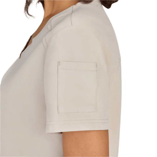 Light beige short-sleeve scrub top in side view with chest pocket and visible seam detailing