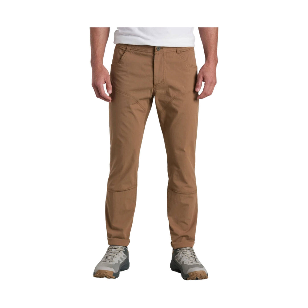 Tan men’s hiking pants with articulated knees and gray trail shoes