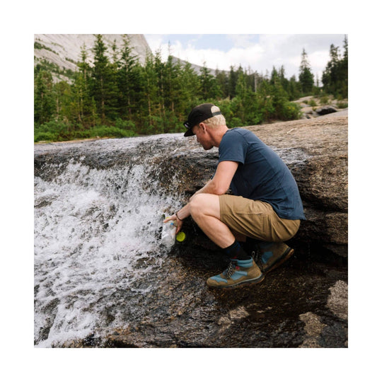 Tan hiking shorts worn by a man crouching on a rock by a stream