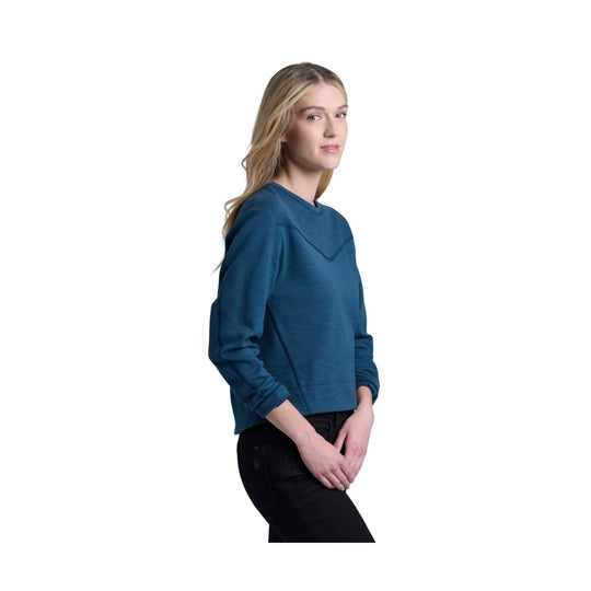 Woman wearing a blue long-sleeve sweatshirt with a V-shaped seam detail and black pants, shown in side view