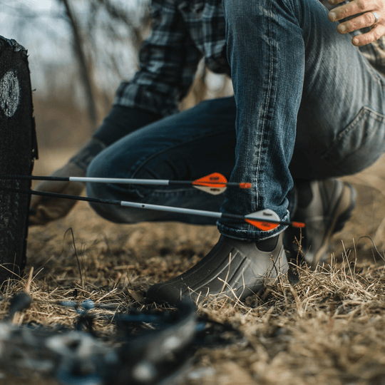 Dark gray mid-height rubber boots on a person kneeling outdoors with arrows in the foreground