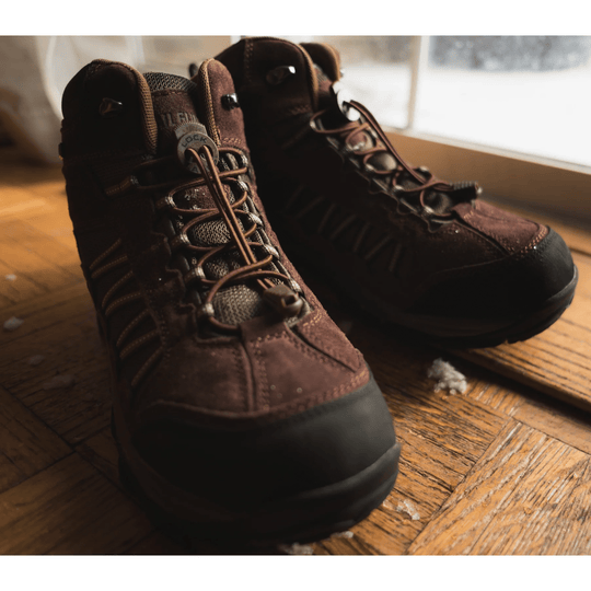 Brown hiking boots with black rubber toe caps, elastic lace system, and padded collars, shown in a pair on a wooden floor