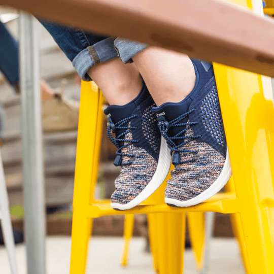 Blue knit athletic shoes with elastic laces on a yellow stool