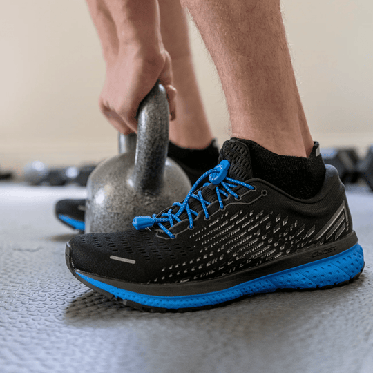 Black athletic shoe with bright blue bungee laces and blue sole being held beside a kettlebell